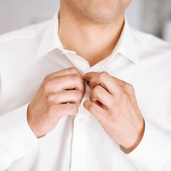 Mann knöpft weißes Hemd zu